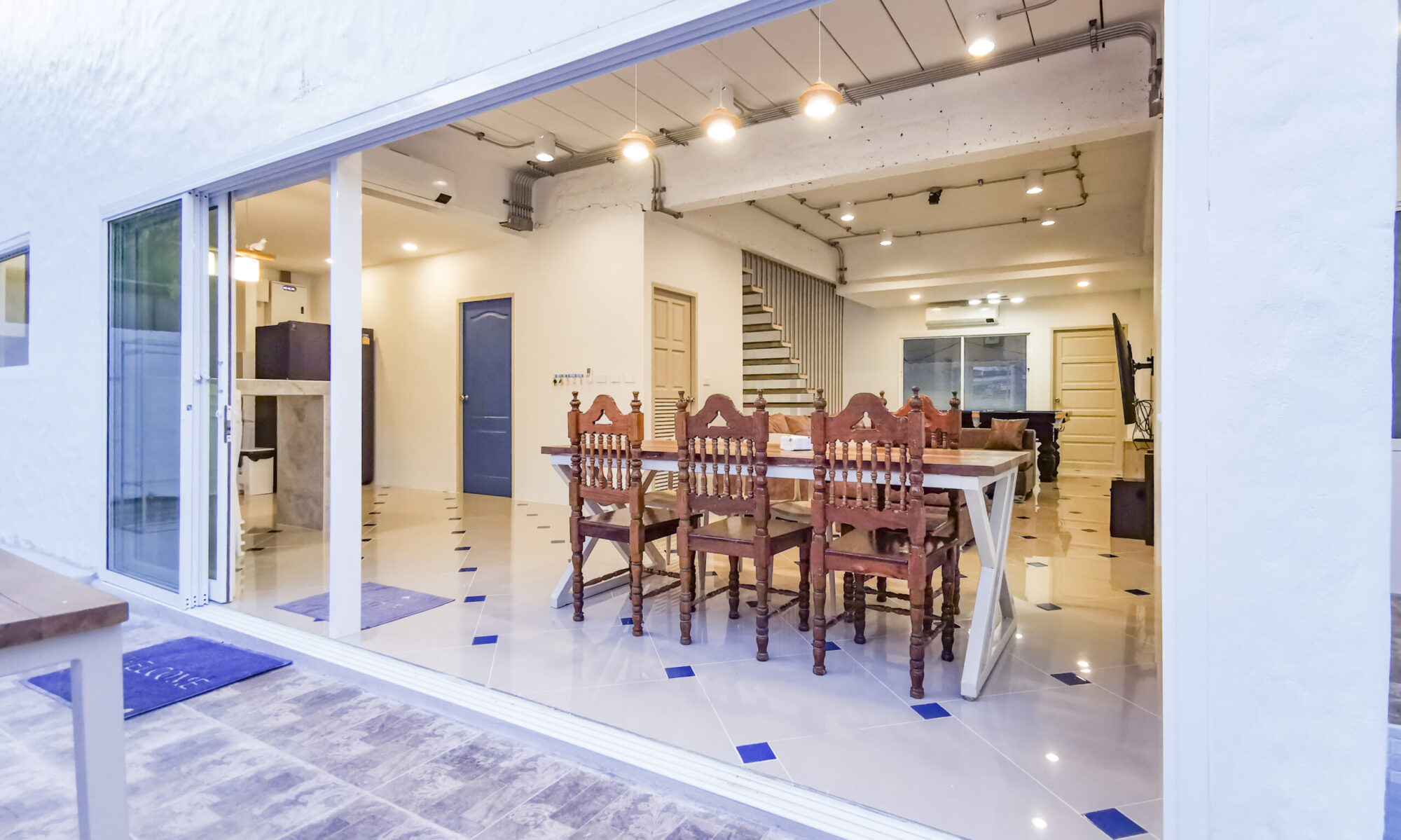 Bright open entrance at Thepprasit Cosy Twin seamless patio-to-dining flow with a long wooden table, blue-accent tiles, and an inviting indoor kitchen.