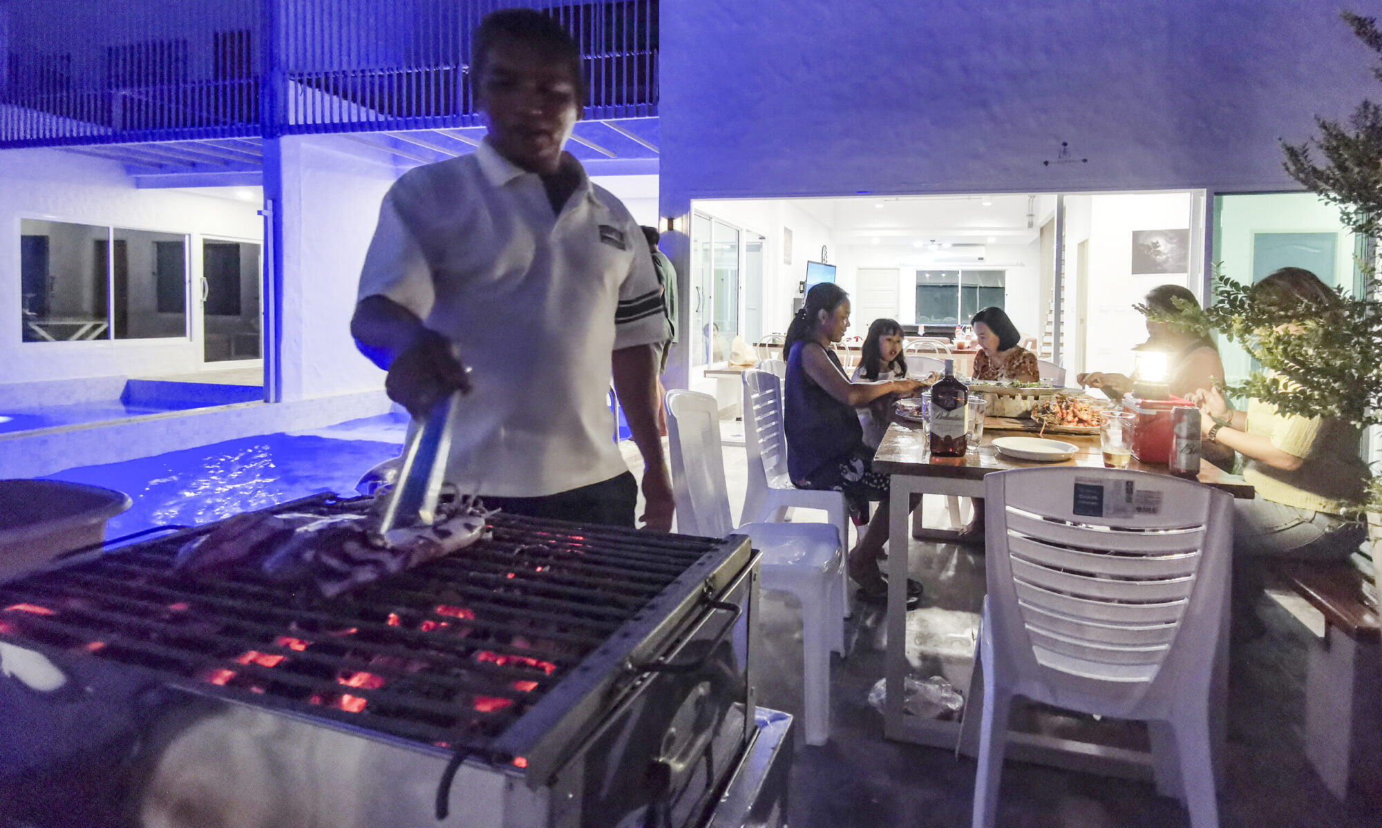 Evening BBQ gathering at Thepprasit Cosy Twin A guests sharing laughter and grilled delights beside the glowing poolside patio.